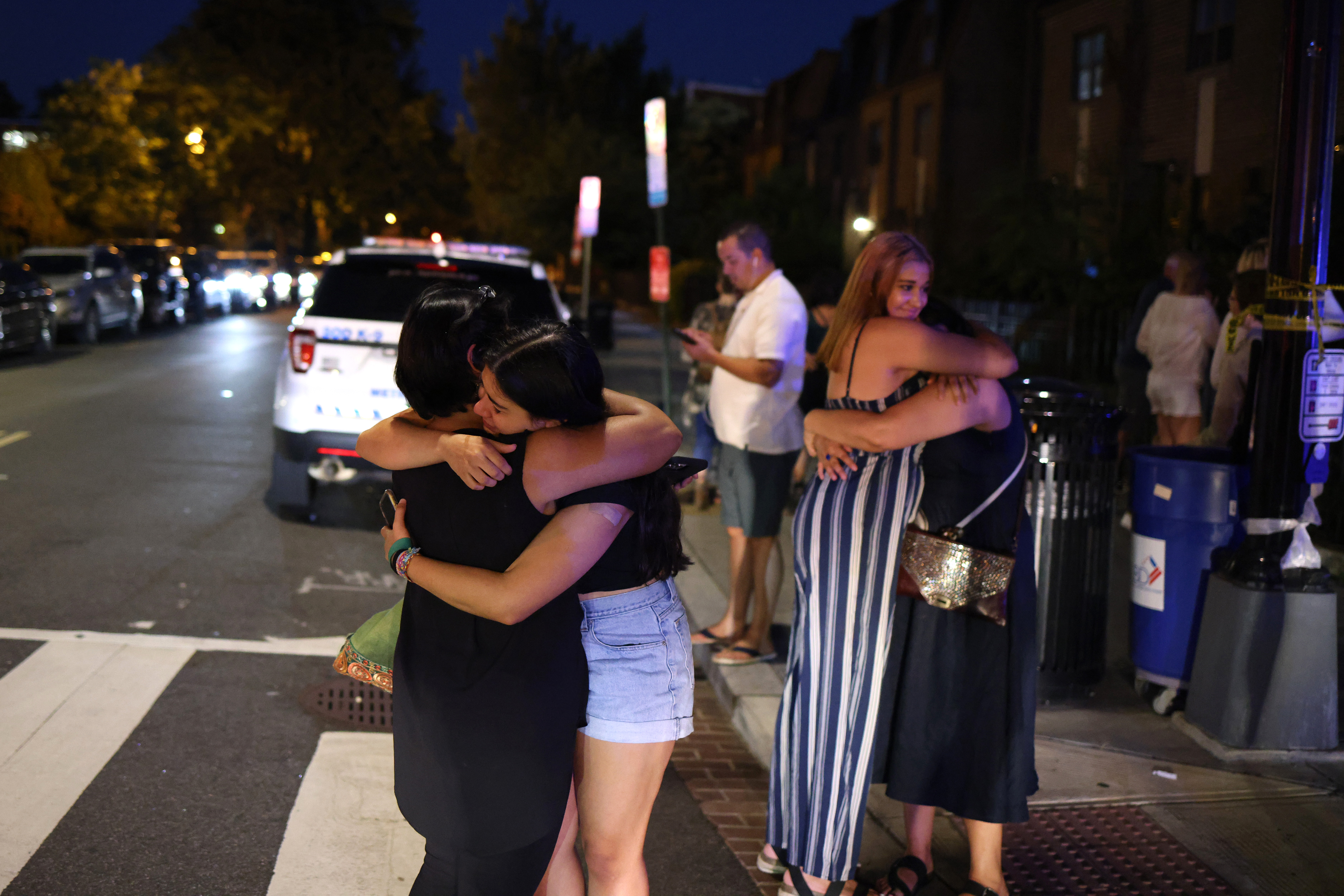 La gente se abraza cerca del sitio de un tiroteo el 22 de julio de 2021 en Washington, DC. Los disparos estallaron en una calle muy transitada, hiriendo a dos y enviando a otros a huir por seguridad. Se buscaba un sedán oscuro en relación con el tiroteo y se esperaba que los dos heridos sobrevivieran, según informes publicados.