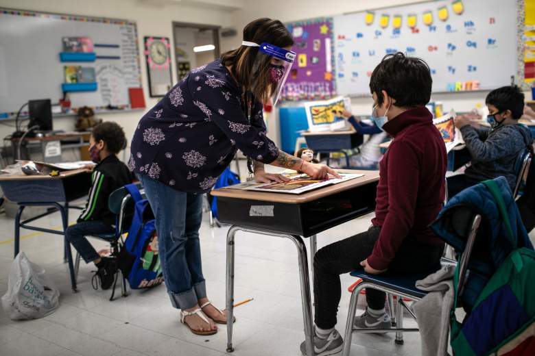 La maestra Elizabeth DeSantis, con una máscara y un protector facial, ayuda a un alumno de primer grado durante la clase de lectura en la Escuela Primaria Stark el 16 de septiembre de 2020 en Stamford, Connecticut.