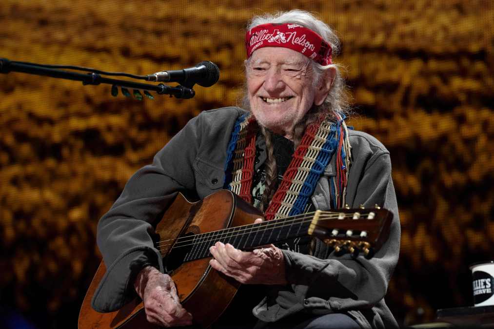 Willie Nelson smiling while holding a guitar