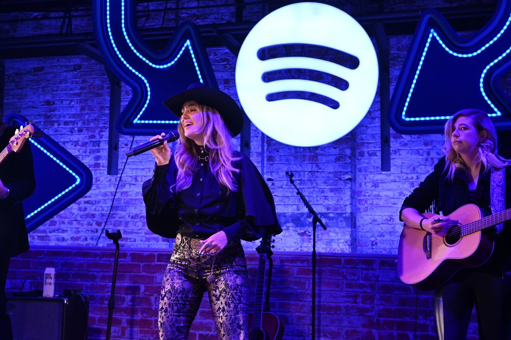 Lainey Wilson singing in front of the Spotify logo